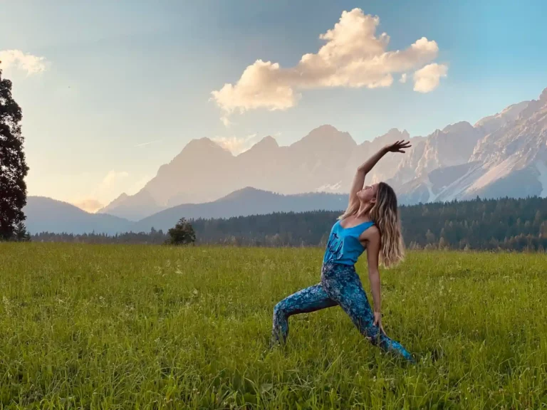 Yogalehrerin in einer Yogahaltung auf einer Wiese vor Bergkulisse