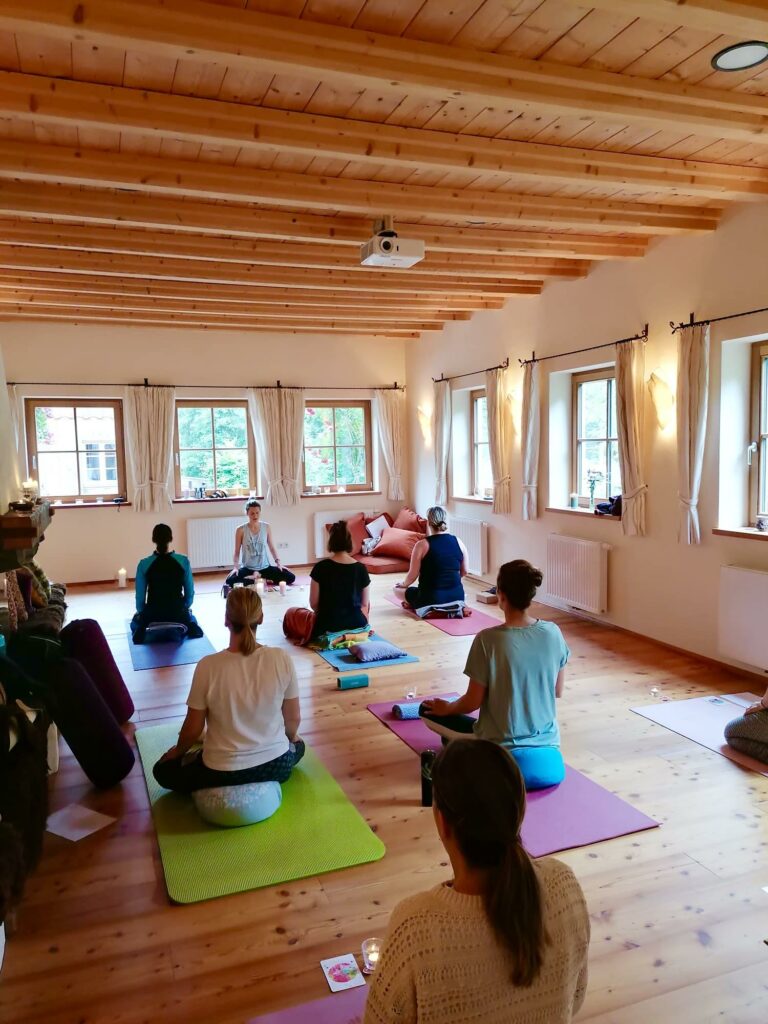 Yoga-Gruppe übt auf bunten Matten in einem hellen Raum mit Holzdecke