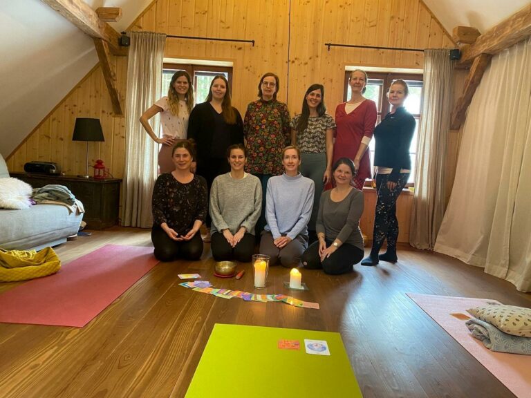 Retreat-Gruppe von zehn Frauen im Yogaraum mit Kerzen und Matten